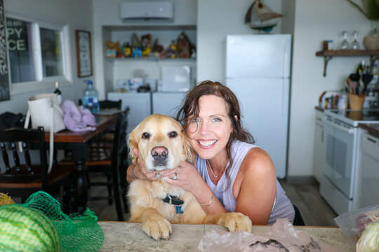Happy woman hugging her golden retriever dog in the kitchen