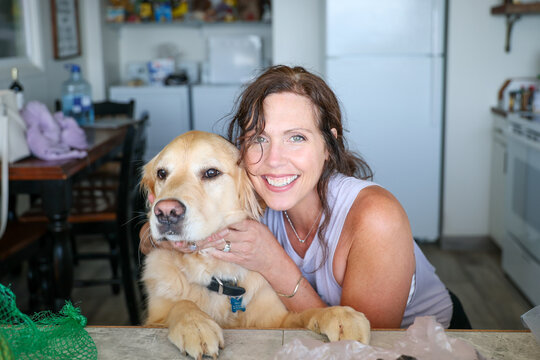 Happy woman hugging her golden retriever dog in the kitchen