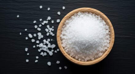 Wooden bowl filled with white salt crystals on black slate background
