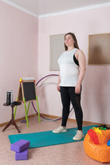 Woman stands in her indoor home workout space during fitness training session. Full length three...