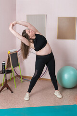 Full length view of an adult female executing dynamic lateral bend, with her arms elevated in perfect posture, segment of domestic pilates routine. Woman is attired in tank top, leggings and sneakers