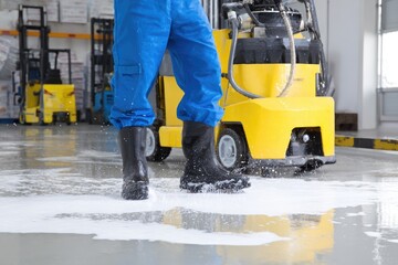 Worker in blue suit cleans factory floor with machine
