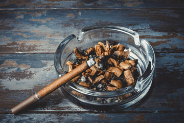 Cigarette with ashtray on wooden background. Burning cigarette in glass ashtray. Tobacco smoking. Tobacco or health. 