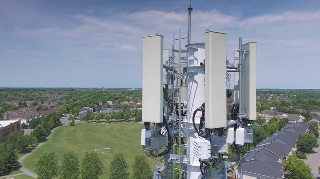 Aerial view of a cellular tower overlooking a suburban neighborhood, surrounded by greenery under a blue sky