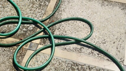 Serpentine Hose Dance on Patterned Patio, Green Tubing Amidst Stone Paving , Garden Hose Lying on...