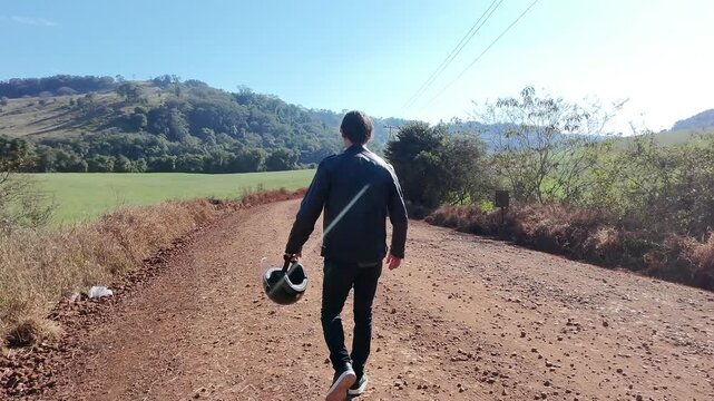 motociclista caminha com capacete em estrada de terra