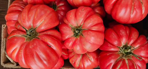 Top-down view of a box filled with ripe ribbed heirloom tomatoes. The deep red color and organic, irregular shapes highlight their natural freshness and garden-grown character.