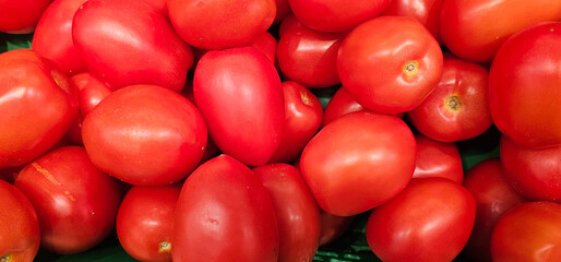 A close-up view of fresh red Roma tomatoes stacked together at a market stall. The vibrant color...