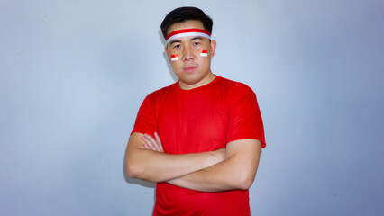 Portrait of a confident young Asian man wearing a red t-shirt and Indonesian flag headband standing with crossed arms. Indonesian Independence Day concept.