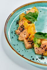 A beautifully arranged dish featuring succulent salmon garnished with fresh herbs, citrus elements, and a touch of savory seasoning on an elegant blue plate.