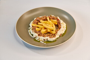 A delicious plate featuring minced meat topped with savory sauce and golden fries, artfully presented on a modern dish, creating an appetizing culinary experience.