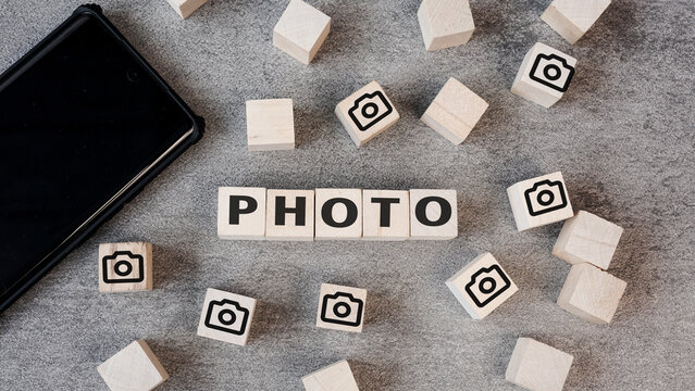 Photography and digital media concept. The word PHOTO on wooden blocks with camera icons and a smartphone on a grey background.