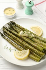 Tasty cooked asparagus served with lemon and thyme on white wooden table, closeup