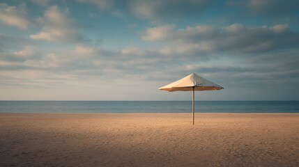 A solitary beach umbrella stands on a calm sandy shore under a cloudy sky with a tranquil sea in the background.