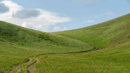 Scenic landscape featuring rolling green hills with a winding dirt path, under a bright blue sky with fluffy clouds, showcasing the beauty of nature and tranquility
