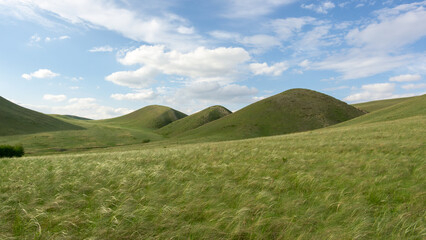 Expansive green hills under a bright blue sky with fluffy clouds, showcasing the beauty of nature and the tranquility of the landscape in a serene environment