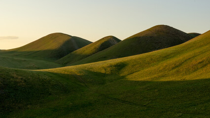 Rolling green hills under a soft golden light create a serene landscape, showcasing the beauty of...
