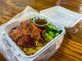 roast duck with egg noodles, dry noodles, and a side of vegetables on a takeout box