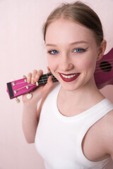 Young female musician holding ukulele by neck and slinging musical instrument over shoulder, she's feeling inspired. Beautiful woman looking camera with smile, positive attitude and happy expression