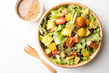 Top view of colorful vegetable salad in wooden bowl with Japanese sesame dressing on white background, Healthy, fresh, plant based eating concept