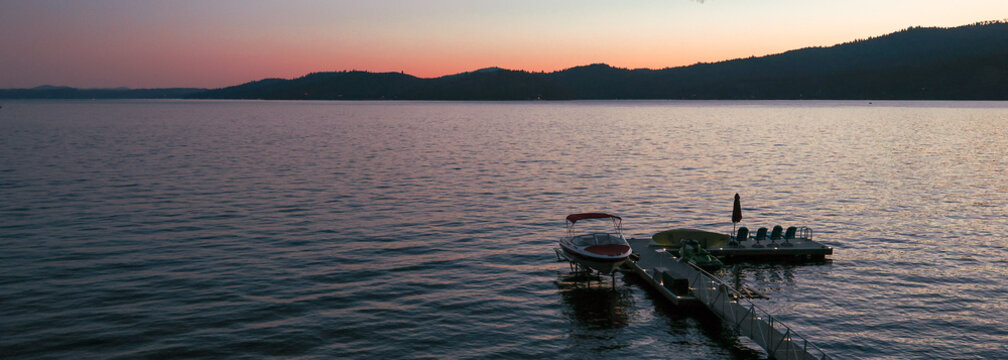 Warm sunset over lake Couer D'Alene in Idaho. Dusk brings a colorful hue in the sky over the pretty water. A boat dock is in the forefront.
