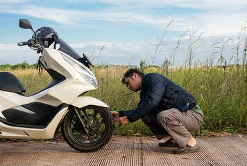 Man checking for a flat tire on his scooter, stranded on a rural road. Roadside assistance photo concept 