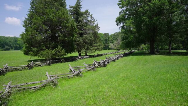 Historic split rail fencing lining a grassy Yorktown battlefield with trees and open fields under a bright summer sky in Yorktown, Virginia.