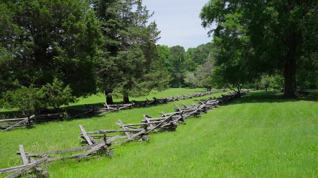 Historic split rail fencing lining a grassy Yorktown battlefield with trees and open fields under a bright summer sky in Yorktown, Virginia.