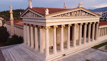 High-angle view of a classical Greek-style building.?Exterior,?with?columns,?pediment,?and?steps.?Surrounded?by?parkland,?with?mountains?in?background.?Soft?light