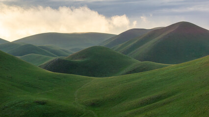 Rolling green hills under a cloudy sky, showcasing the beauty of nature's landscape, with soft curves and vibrant colors creating a serene atmosphere of tranquility and peace