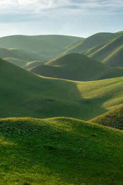Rolling green hills under a bright sky create a serene landscape, showcasing the beauty of nature with gentle slopes and vibrant grass, inviting exploration and tranquility