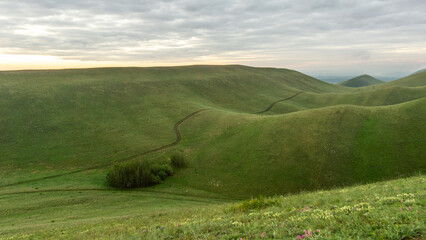 Expansive green hills under a cloudy sky, showcasing rolling landscapes with gentle slopes and a serene atmosphere, perfect for nature lovers and outdoor enthusiasts seeking tranquility