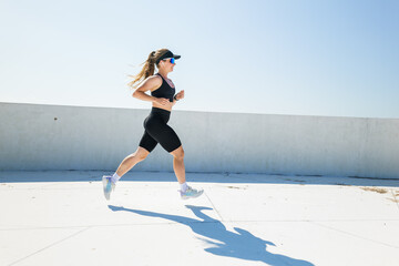 Active woman jogging on rooftop under clear blue sky