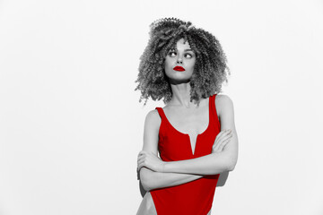 Stunning model with curly hair in a striking red swimsuit poses confidently against a minimalist...