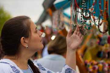 Young adult white brunette woman chooses jewelry, beads, handmade accessories for gift at street christmas fair, Tbilisoba city festival, autumn holiday, New year market. Concept of jewelry, tourism