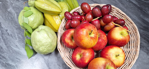 Apples, starfruits, dates, guavas in a white wooden basket on a marble table.