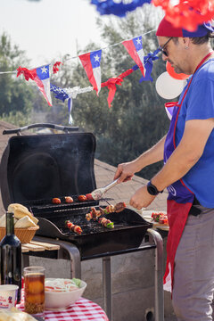 Chilean Independence Day: man grilling meat skewers and chorizos at festive barbecue &ndash; vertical
