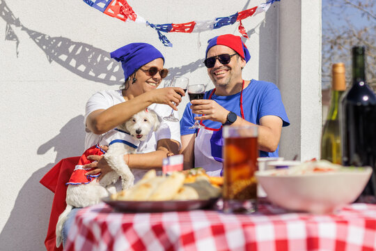 Chilean Independence Day: Couple toasting with wine next to traditional food and dog in costume