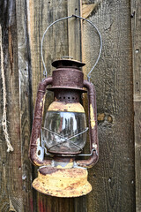 Old rusty lantern with glass chamber hanging on a weathered wooden wall. Vintage rustic charm perfect for themes of countryside living, nostalgia, retro decor, or historical outdoor ambiance.