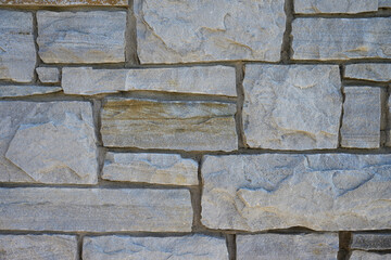 Close-up of a grey stone wall with stacked rectangular blocks and natural textures. Ideal for architectural backgrounds, construction themes, or design templates with a rustic stone aesthetic.