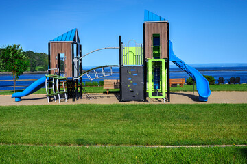 Modern playground with blue slides and climbing features set in a seaside park on a sunny day. Perfect for concepts of family fun, childhood, recreation, and outdoor community spaces.