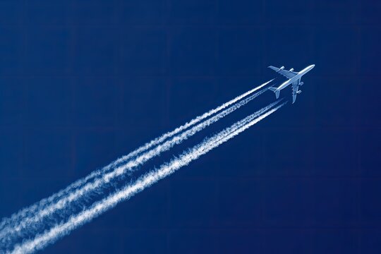Airplane in flight, contrails against deep blue sky - Powered by Adobe