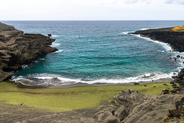 A scenic view of Green Sand Beach on Hawaii’s Big Island, where rare olive-green sand meets rugged volcanic cliffs and deep blue ocean.