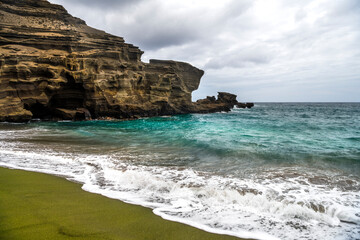 A scenic view of Green Sand Beach on Hawaii&rsquo;s Big Island, where rare olive-green sand meets rugged volcanic cliffs and deep blue ocean.
