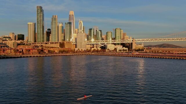 A lone kayaker paddles on the bay in San Francisco, California, USA, with the city skyline and Bay Bridge in the background, enjoying the peace and exercise.