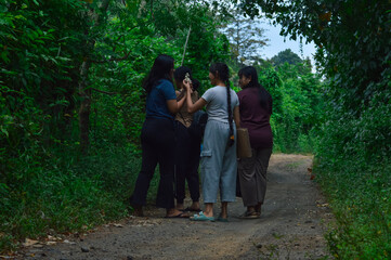 Amid the thick greenery of the forest, the girls gently pick small wildflowers from the side of the...