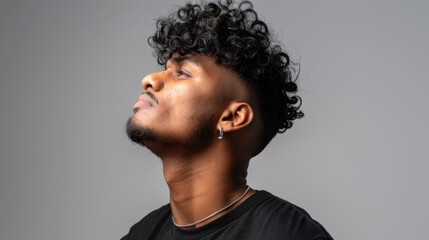 Obraz premium Curly hairstyle with mid fade cut, showcasing defined curls and confident expression. individual is wearing simple black shirt and silver necklace, creating stylish look
