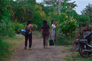 The girls stop briefly by a small flower-filled clearing near a parked motorbike area, observing...