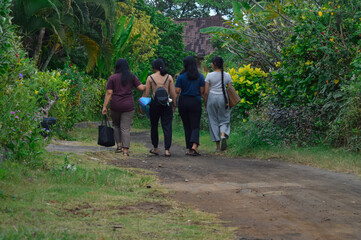 Fototapeta premium The girls walk side by side through a garden trail, quietly observing the plants and atmosphere along the dirt path.