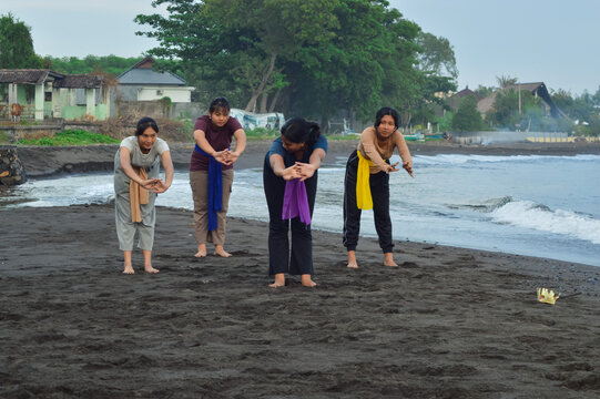 The four girls bend forward in yoga with fingers interlocked and palms stretching straight ahead while facing forward on the sand.